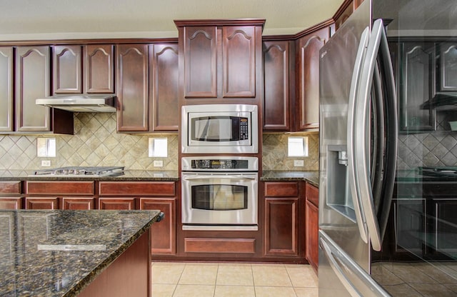 11704 Shoal Lndg, Pearland, TX 77584 - kitchen with appliances with stainless steel finishes, reddish brown cabinets, under cabinet range hood, dark stone countertops, and decorative backsplash