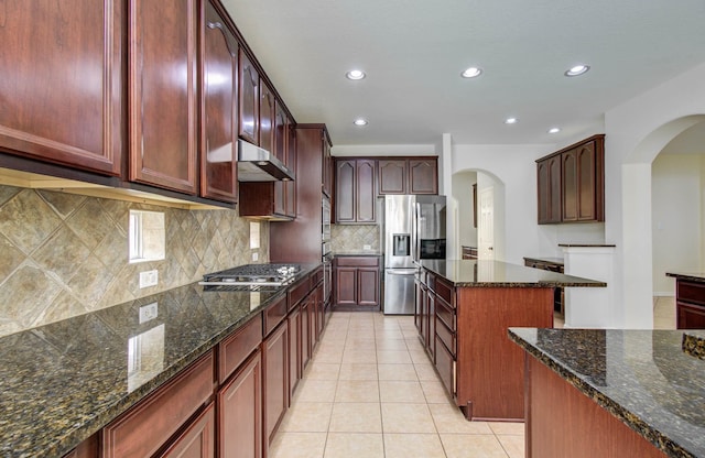 11704 Shoal Lndg, Pearland, TX 77584 - kitchen featuring stainless steel appliances, arched walkways, under cabinet range hood, dark stone countertops, and recessed lighting