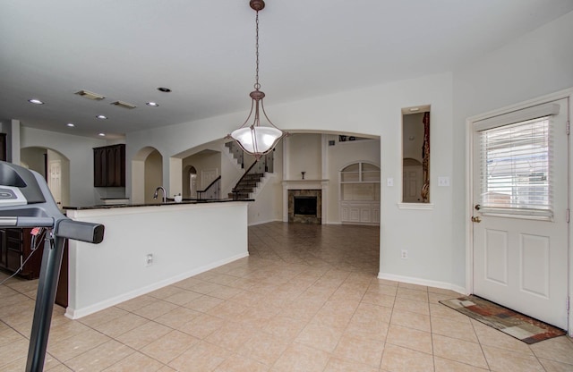 11704 Shoal Lndg, Pearland, TX 77584 - kitchen featuring arched walkways, light tile patterned floors, dark countertops, pendant lighting, and a fireplace