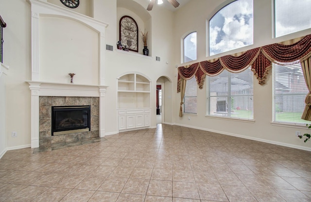11704 Shoal Lndg, Pearland, TX 77584 - unfurnished living room with built in shelves, ceiling fan, a tiled fireplace, a high ceiling, and light tile patterned flooring