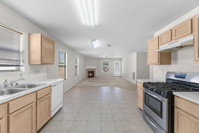 16810 Perryton Ln, Houston, TX 77073 - kitchen with stainless steel range with gas cooktop, light brown cabinetry, under cabinet range hood, dishwasher, and a warm lit fireplace
