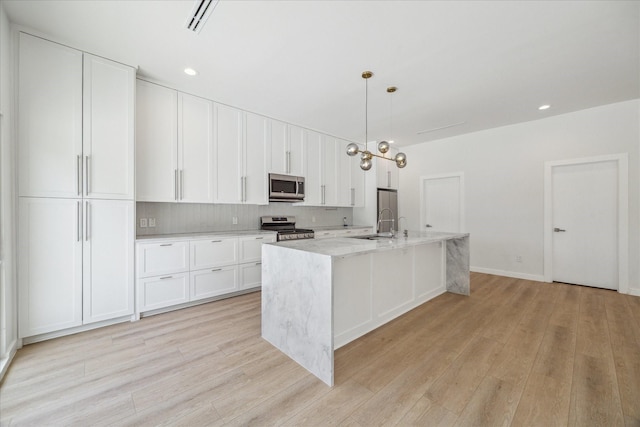 10225 Shadow Oaks Dr, Houston, TX 77043 - kitchen featuring appliances with stainless steel finishes, light wood finished floors, a kitchen island with sink, white cabinetry, and recessed lighting