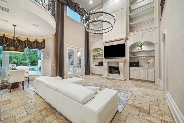 6 Kings Lake Estates Blvd, Kingwood, TX 77346 - living room featuring built in features, stone tile flooring, a towering ceiling, a chandelier, and a fireplace with raised hearth