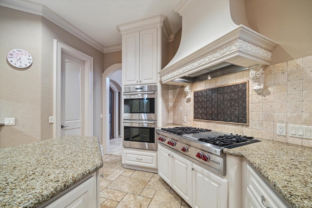 6 Kings Lake Estates Blvd, Kingwood, TX 77346 - kitchen featuring appliances with stainless steel finishes, premium range hood, backsplash, arched walkways, and light stone counters