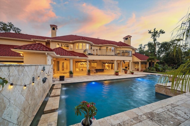 6 Kings Lake Estates Blvd, Kingwood, TX 77346 - back of house at dusk featuring a balcony, a chimney, ceiling fan, a patio area, and an outdoor pool