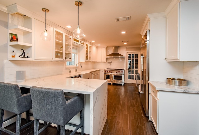327 Cinnamon Oak Ln, Houston, TX 77079 - kitchen featuring range with two ovens, wall chimney exhaust hood, a peninsula, light stone countertops, and glass insert cabinets