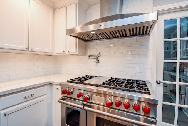 327 Cinnamon Oak Ln, Houston, TX 77079 - kitchen with wall chimney exhaust hood, range with two ovens, backsplash, white cabinetry, and light stone counters