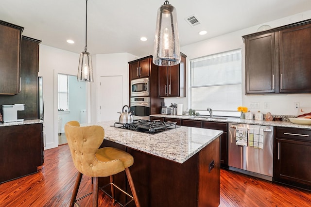 2209 Bastrop St, Houston, TX 77003 - kitchen with appliances with stainless steel finishes, a center island, dark brown cabinets, dark wood-style floors, and light stone countertops