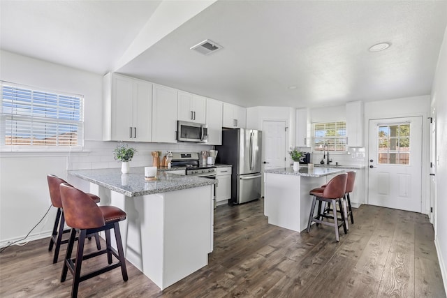 605 Waco St, Dayton, TX 77535 - kitchen featuring appliances with stainless steel finishes, a kitchen bar, decorative backsplash, white cabinets, and light stone countertops