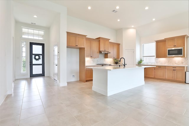 24526 Bluestar Blossom Trl, Katy, TX 77493 - kitchen with stainless steel microwave, a towering ceiling, light countertops, backsplash, and an island with sink
