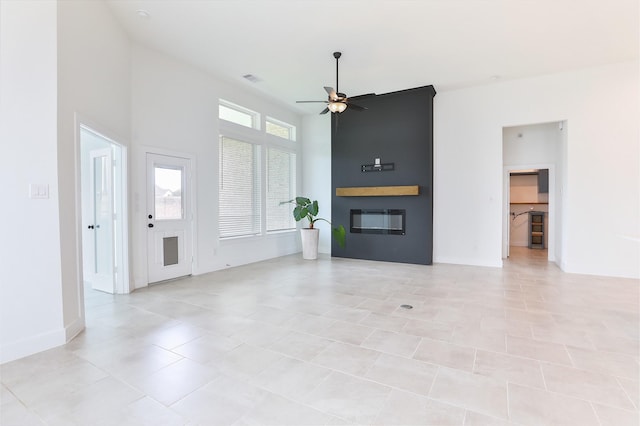 24526 Bluestar Blossom Trl, Katy, TX 77493 - unfurnished living room featuring a ceiling fan, a large fireplace, a high ceiling, and light tile patterned flooring