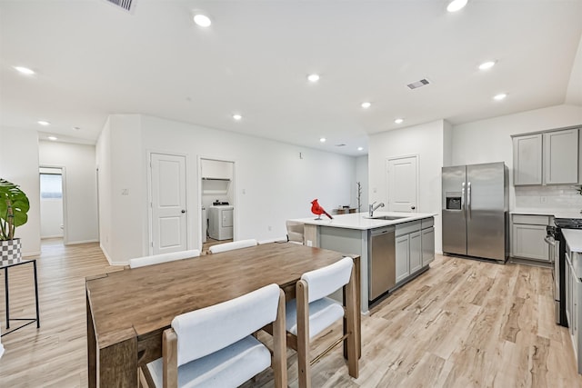 19911 Paros Island Dr, Hockley, TX 77447 - kitchen featuring appliances with stainless steel finishes, gray cabinetry, washer / clothes dryer, an island with sink, and light wood-style floors