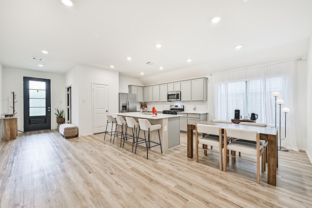 19911 Paros Island Dr, Hockley, TX 77447 - kitchen with stainless steel appliances, an island with sink, a kitchen bar, gray cabinets, and light wood-style flooring