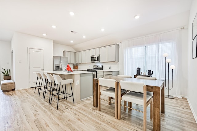 19911 Paros Island Dr, Hockley, TX 77447 - kitchen featuring appliances with stainless steel finishes, a center island, a breakfast bar, gray cabinetry, and light wood-type flooring