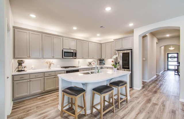 15023 Eves Necklace Ct, Cypress, TX 77433 - kitchen featuring stainless steel appliances, gray cabinets, arched walkways, a breakfast bar, and light wood-style flooring