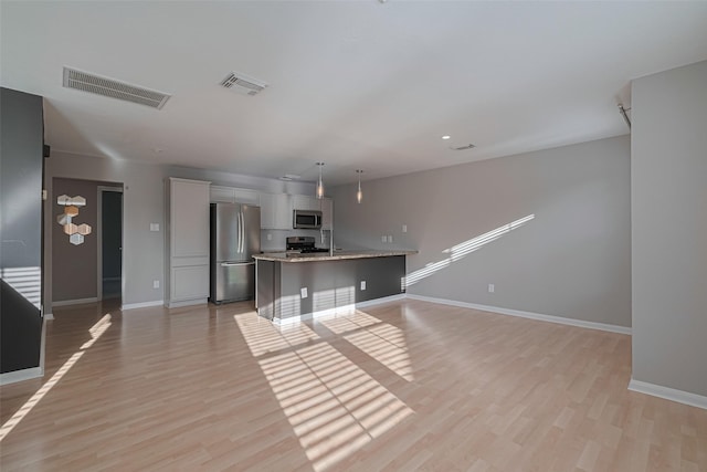1101 Saulnier St, Houston, TX 77019 - kitchen featuring appliances with stainless steel finishes, white cabinets, light wood-style flooring, a kitchen island with sink, and hanging light fixtures