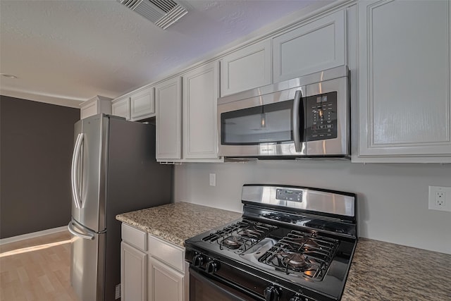 1101 Saulnier St, Houston, TX 77019 - kitchen with stainless steel appliances, white cabinetry, wood finished floors, and light stone counters