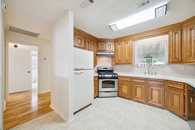 3006 Hartwick Rd, Houston, TX 77093 - kitchen featuring freestanding refrigerator, stainless steel gas range, under cabinet range hood, and brown cabinets