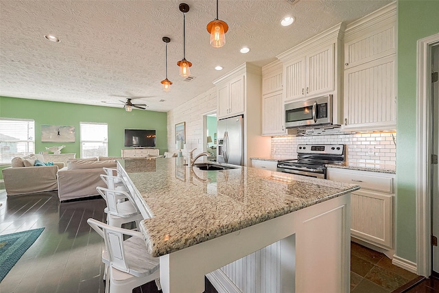3401 Sand Castle Ln, Port Bolivar, TX 77650 - kitchen featuring appliances with stainless steel finishes, ceiling fan, a textured ceiling, open floor plan, and a kitchen breakfast bar