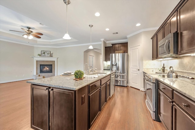 716 Saturnia Ln, League City, TX 77573 - kitchen featuring appliances with stainless steel finishes, light wood finished floors, arched walkways, a ceiling fan, and dark brown cabinets