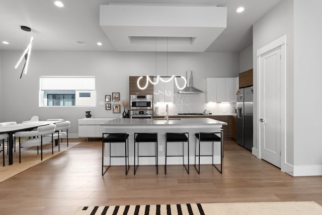1617 Wheeler St Unit C, Houston, TX 77004 - kitchen featuring wall chimney range hood, stainless steel appliances, a kitchen breakfast bar, white cabinetry, and light wood-style floors