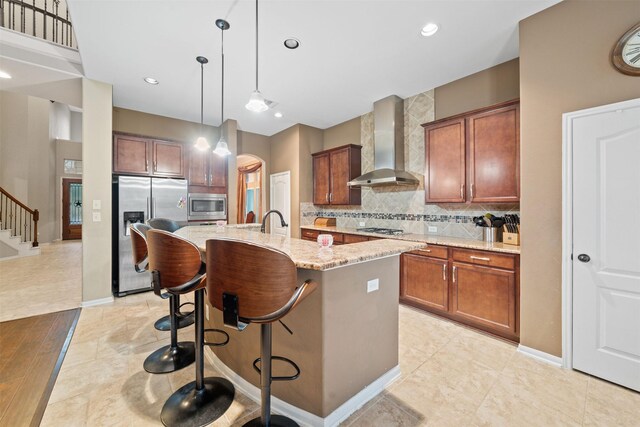 4314 Walden Terrace Ln, Humble, TX 77396 - kitchen with wall chimney exhaust hood, stainless steel appliances, decorative backsplash, light stone counters, and a kitchen island with sink