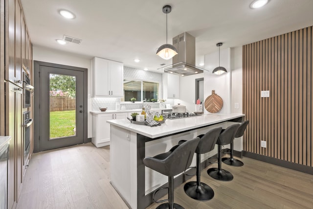 5425 Viking Dr, Houston, TX 77092 - kitchen featuring island range hood, light wood finished floors, a breakfast bar area, white cabinetry, and recessed lighting