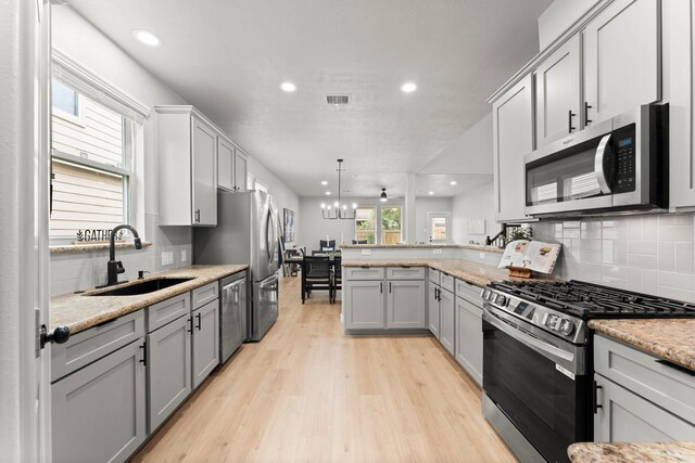 30742 Gardenia Trace Dr, Spring, TX 77386 - kitchen featuring appliances with stainless steel finishes, a peninsula, gray cabinetry, backsplash, and light wood-type flooring