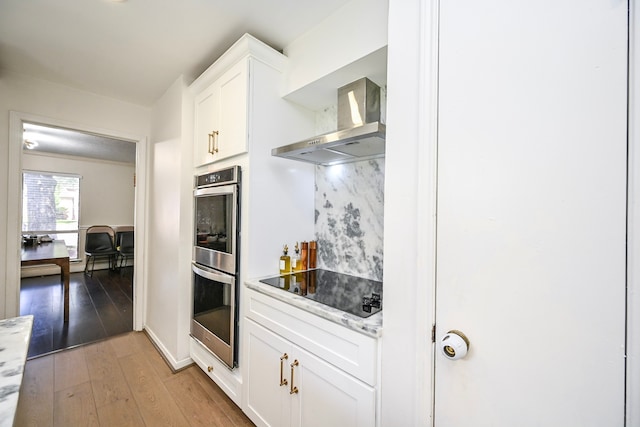 11811 Braesridge Dr, Houston, TX 77071 - kitchen featuring wall chimney range hood, double oven, black electric cooktop, white cabinetry, and light wood finished floors