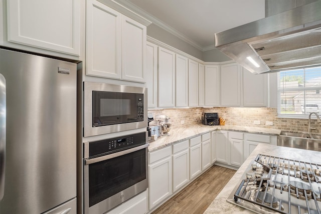 12118 Enclave Ct, Santa Fe, TX 77510 - kitchen with stainless steel appliances, exhaust hood, white cabinetry, decorative backsplash, and light wood-type flooring