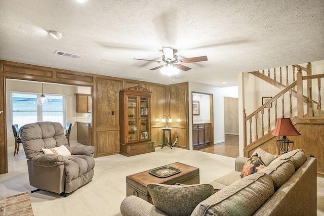 22419 Kent Falls Dr, Katy, TX 77450 - living room featuring ceiling fan, stairs, wooden walls, a textured ceiling, and light colored carpet