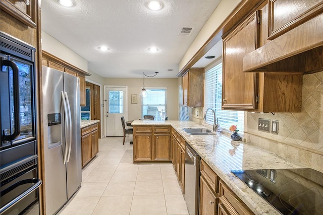 22419 Kent Falls Dr, Katy, TX 77450 - kitchen with stainless steel appliances, a peninsula, brown cabinetry, tasteful backsplash, and light stone counters