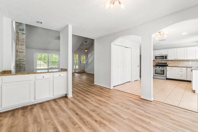 6 Fairmeade Bend Dr, The Woodlands, TX 77381 - kitchen with appliances with stainless steel finishes, light wood-type flooring, white cabinetry, arched walkways, and backsplash