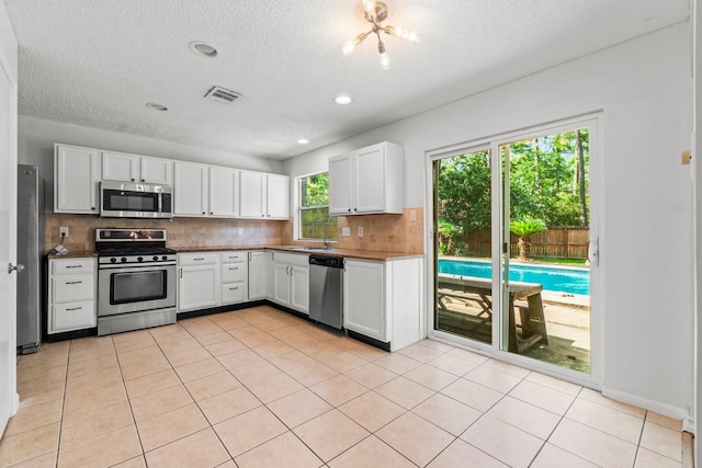 6 Fairmeade Bend Dr, The Woodlands, TX 77381 - kitchen with stainless steel appliances, decorative backsplash, white cabinetry, a textured ceiling, and light tile patterned flooring