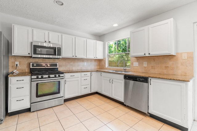 6 Fairmeade Bend Dr, The Woodlands, TX 77381 - kitchen featuring appliances with stainless steel finishes, white cabinetry, a textured ceiling, light stone counters, and tasteful backsplash