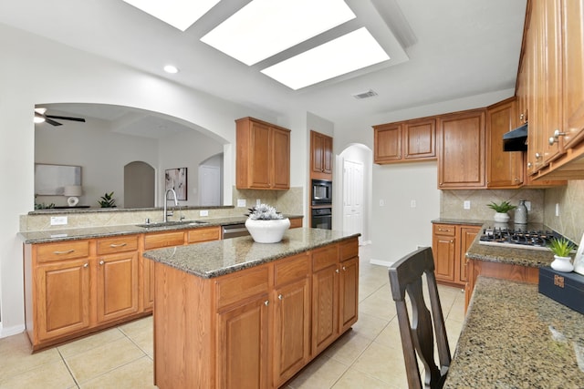 6538 Ivy Heath Ln, Houston, TX 77041 - kitchen featuring light tile patterned flooring, arched walkways, a center island, stone counters, and brown cabinetry