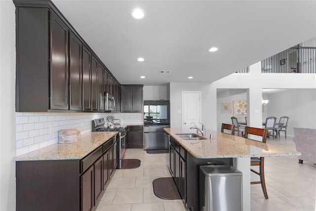 18519 Orono Ridge Trl, Richmond, TX 77407 - kitchen with appliances with stainless steel finishes, a kitchen bar, backsplash, light stone countertops, and dark brown cabinets