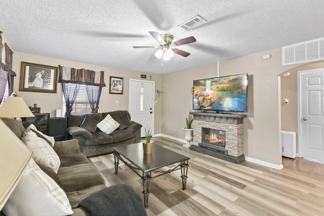 315 E Adoue St, Baytown, TX 77520 - living area featuring ceiling fan, light wood-style floors, arched walkways, a textured ceiling, and a stone fireplace