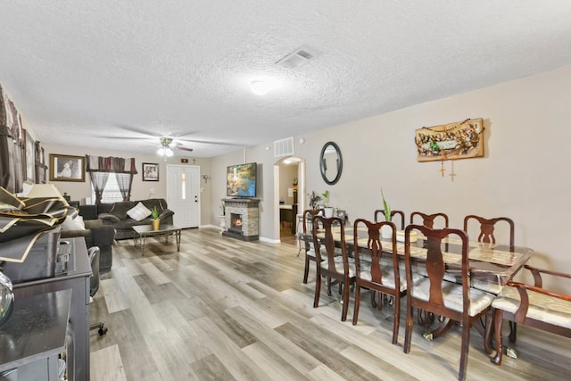 315 E Adoue St, Baytown, TX 77520 - dining space featuring ceiling fan, a textured ceiling, light wood-style flooring, arched walkways, and a warm lit fireplace