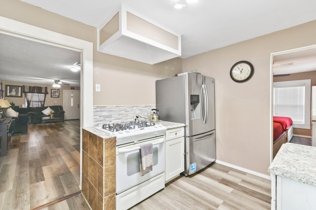 315 E Adoue St, Baytown, TX 77520 - kitchen featuring white gas range, stainless steel fridge, light wood-type flooring, a ceiling fan, and backsplash