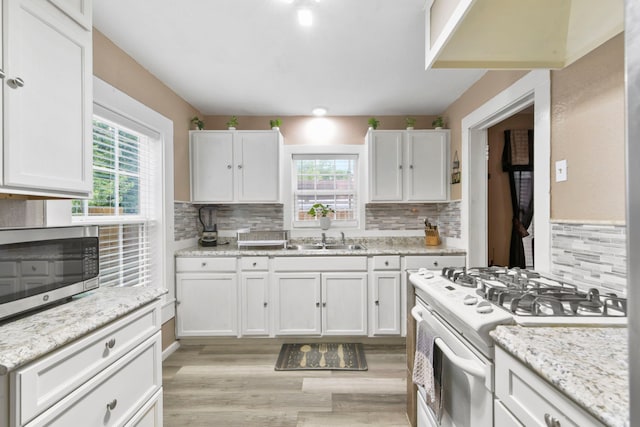 315 E Adoue St, Baytown, TX 77520 - kitchen with white range with gas stovetop, stainless steel microwave, backsplash, light wood-style flooring, and white cabinets
