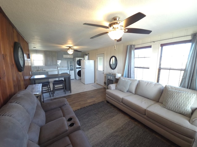 714 Caisson St, Surfside Beach, TX 77541 - living room featuring stacked washer / drying machine, light wood-style flooring, ceiling fan, a textured ceiling, and wooden walls