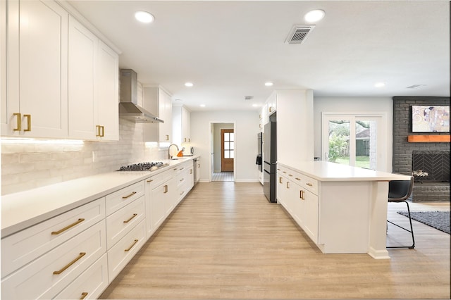 1711 Mossy Stone Dr, Houston, TX 77077 - kitchen with wall chimney range hood, a breakfast bar, light wood-type flooring, a brick fireplace, and tasteful backsplash
