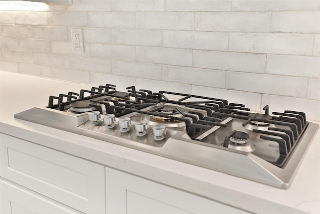 1711 Mossy Stone Dr, Houston, TX 77077 - kitchen view of decorative backsplash, light countertops, stainless steel gas stovetop, and white cabinetry