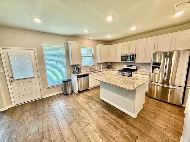 18534 Ariat Dr, Cypress, TX 77429 - kitchen with appliances with stainless steel finishes, light wood finished floors, white cabinets, light stone countertops, and decorative backsplash