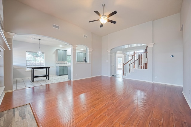 3402 Santa Catalina Ct, Katy, TX 77450 - unfurnished living room featuring ceiling fan, light wood-style flooring, decorative columns, a towering ceiling, and stairway