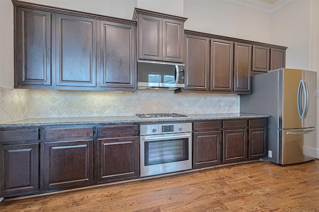1035 E 28th St, Houston, TX 77009 - kitchen with stainless steel appliances, ornamental molding, dark brown cabinets, dark stone counters, and backsplash