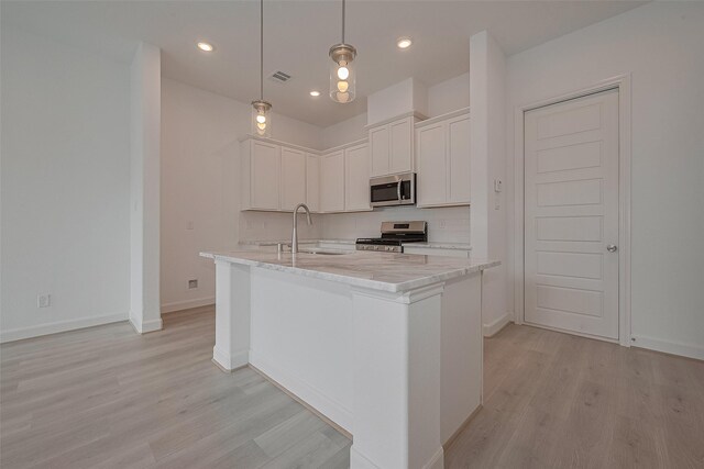 1611 Regents Gate Ct, Houston, TX 77055 - kitchen with stainless steel appliances, light wood-type flooring, white cabinets, a kitchen island with sink, and decorative backsplash
