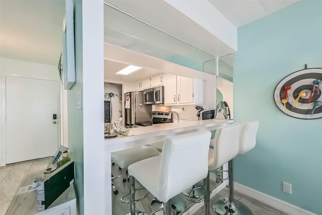 7310 Seawall Blvd Unit 404, Galveston, TX 77551 - kitchen with stainless steel microwave, stove, a kitchen bar, white cabinetry, and light countertops