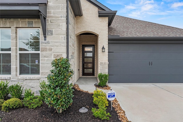 9418 Whispering Bald Cypress Ct, Cypress, TX 77433 - doorway to property featuring a shingled roof, concrete driveway, a garage, brick siding, and stone siding